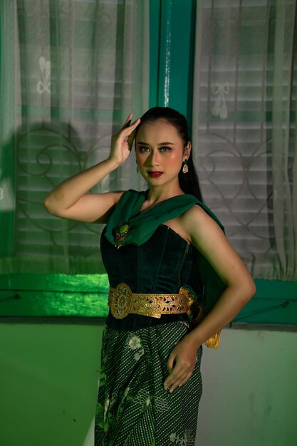 Een vrouwelijke Balinese danseres, helemaal in het groen gekleed, poseert erg sexy in een groene kamer