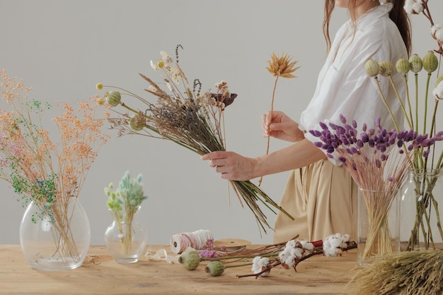 Een vrouwelijke bloemist maakt een eeuwigdurend boeket droogbloemen aan een houten tafel in haar atelier