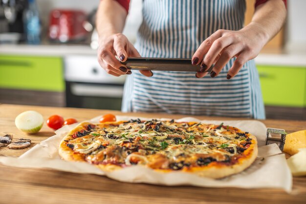 Een vrouwelijke blogger maakt foto's van zelfgemaakte pizza's op haar telefoon