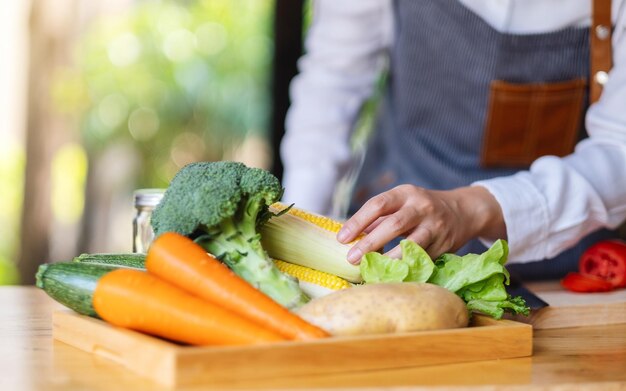 Een vrouwelijke chef-kok die een verse maïs vasthoudt en plukt uit een groentelade op tafel