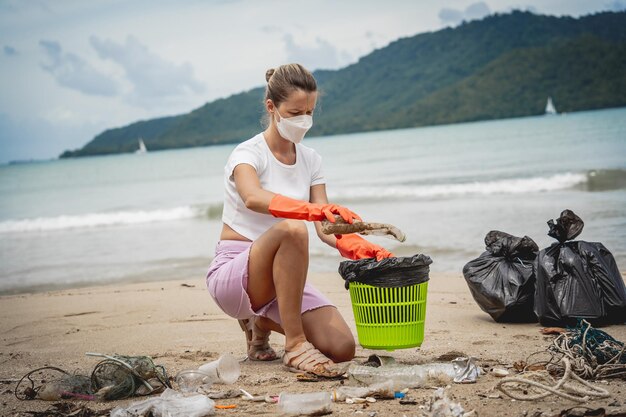 Een vrouwelijke ecoloog-vrijwilliger maakt het strand aan de kust schoon van plastic en ander afval