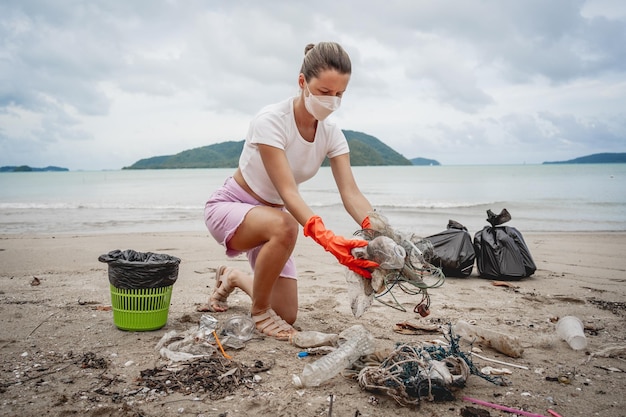 Een vrouwelijke ecoloog-vrijwilliger maakt het strand aan de kust schoon van plastic en ander afval
