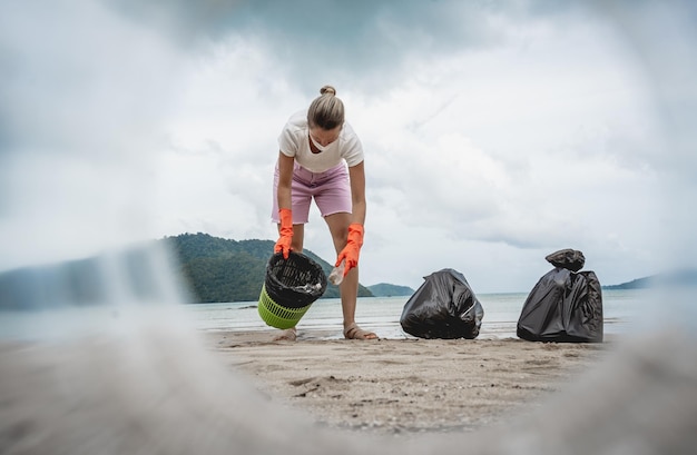 Een vrouwelijke ecoloog-vrijwilliger maakt het strand aan de kust schoon van plastic en ander afval