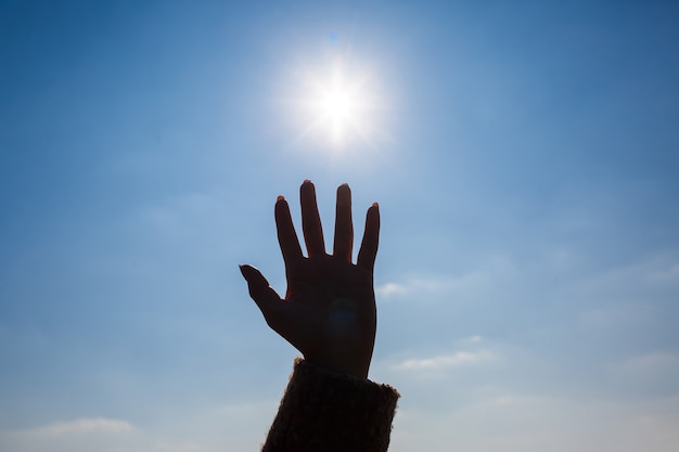 Een vrouwelijke hand afgetekend tegen een blauwe lucht en een felle zon