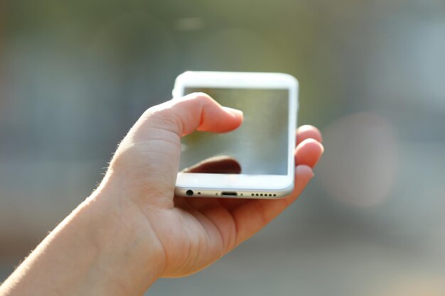 Een vrouwelijke hand die een mobiele telefoon buiten vasthoudt op een onscherpe achtergrond