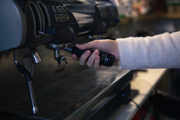 Een vrouwelijke hand houdt een houder vast in een professionele koffiemachine