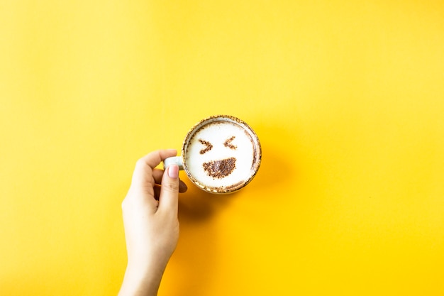 Een vrouwelijke hand houdt een kop van koffie waarop getrokken emoji-gelach
