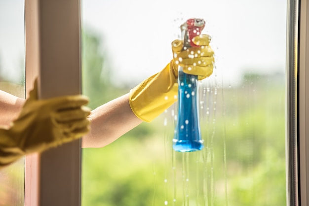 Een vrouwelijke hand in een gele handschoen wast het raam in de zomer. Rasp in de hand. huis schoonmaken