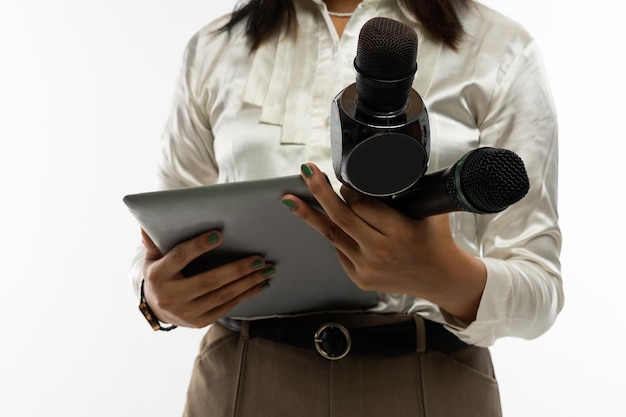 Foto een vrouwelijke journalist in witte blouse met twee microfoons en een tablet bij haar hand