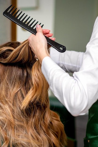 Een vrouwelijke kapper kamt het lange bruine haar van een jonge vrouw in een salon.