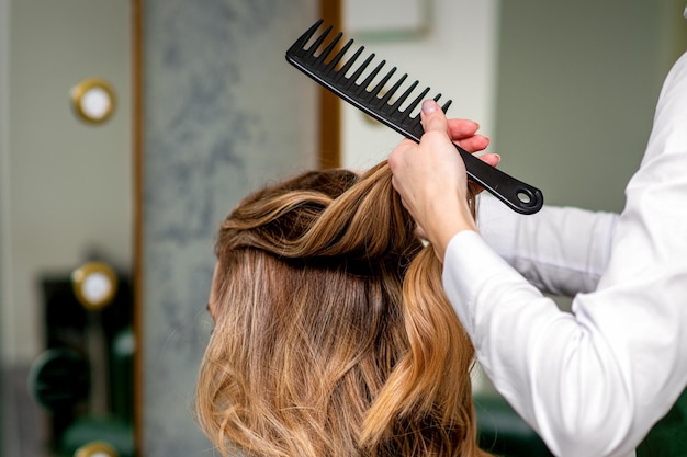 Een vrouwelijke kapper kamt het lange bruine haar van een jonge vrouw in een salon.