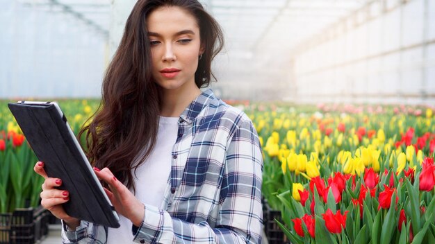 Een vrouwelijke kasmedewerker inspecteert tulpen en voert gegevens in op een tablet