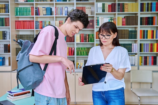 Een vrouwelijke leraar van middelbare leeftijd die met een mannelijke student praat in de bibliotheek.