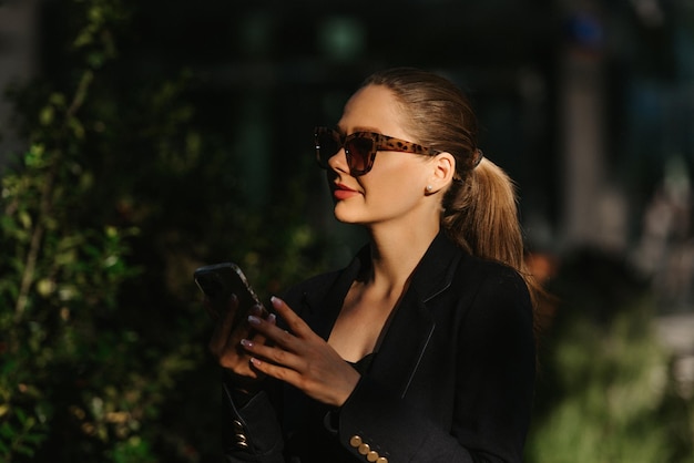 Een vrouwelijke makelaar in een blazer houdt een telefoon vast in de moderne tuin bij zonsondergang