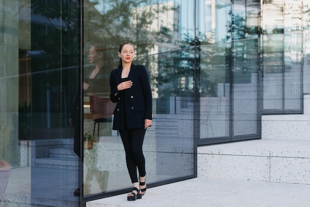 Een vrouwelijke makelaar in een blazer leunt tegen de glazen wand