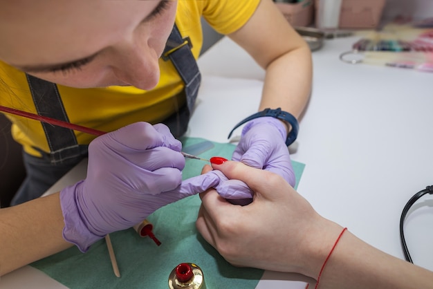 Een vrouwelijke meester schildert nagels met rode vernis voor een klant in een manicure in de salon. Nagelverzorging concept.