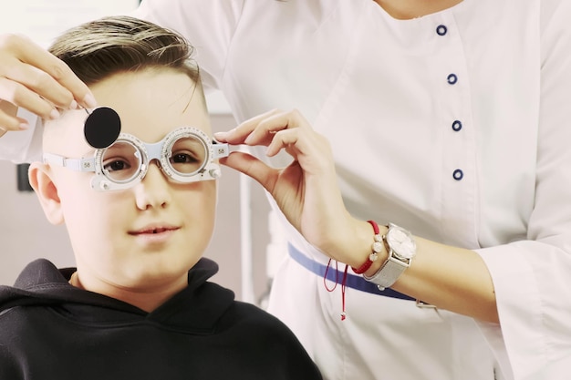 Een vrouwelijke optometrist zet een phoropter op een tienerjongen Oogonderzoek in de oogheelkundige kliniek