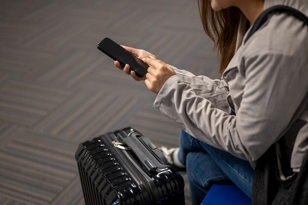 Een vrouwelijke passagier gebruikt haar smartphone terwijl ze op een wachtstoel op de luchthaven zit.