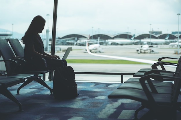 Een vrouwelijke reiziger die een laptop gebruikt terwijl hij op de luchthaven zit