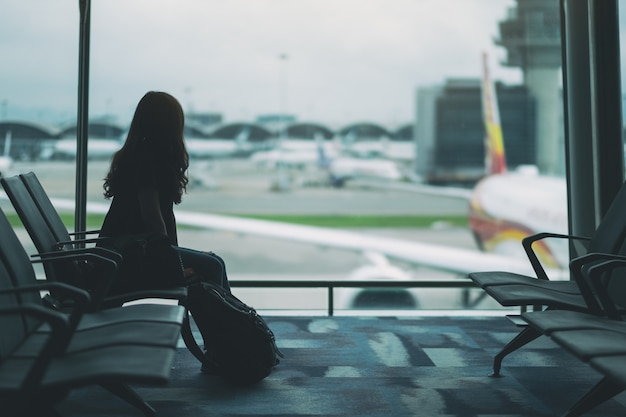 Een vrouwelijke reiziger zit en wacht met rugzak op de luchthaven