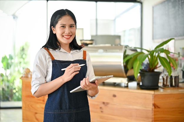 Een vrouwelijke serveerster staat met haar digitale tablet voor de balie van de coffeeshop