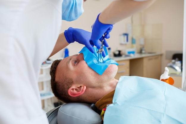 Een vrouwelijke tandarts behandelt tandbederf op de tanden van een mannelijke patiënt in een tandheelkundige kliniek tijdens de coronaviruspandemie. Selectieve focus