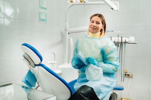 Een vrouwelijke tandarts met een medisch masker en rubberen handschoenen in haar handen zit in haar kantoor.