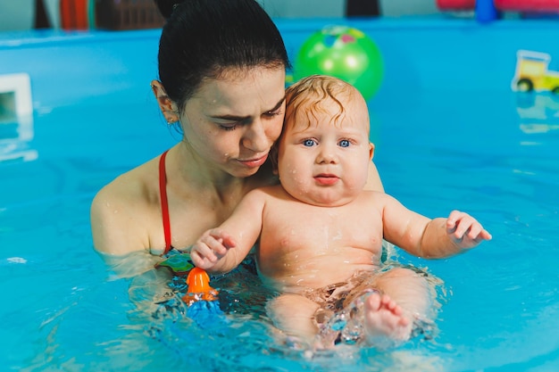 Een vrouwelijke trainer leert een baby zwemmen in het zwembad en ondersteunt zijn handen Babyzwemmen in het zwembad Een pasgeboren jongen leren zwemmen in het zwembad