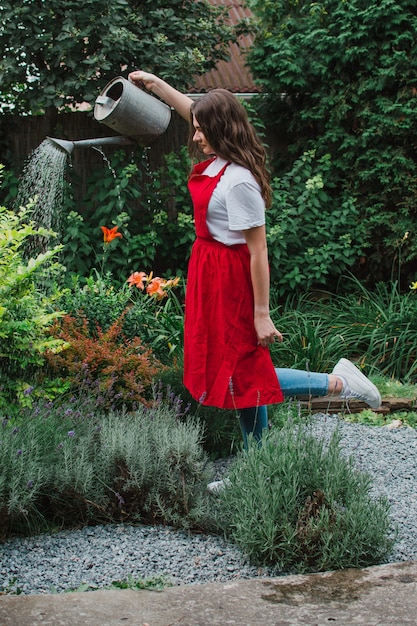 Een vrouwelijke tuinman in een rood schort die de tuin water geeft