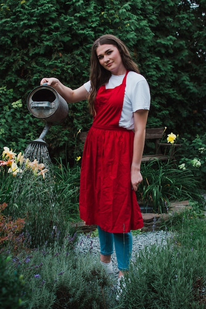 Een vrouwelijke tuinman in een rood schort die de tuin water geeft