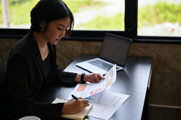Een vrouwelijke uitvoerend manager in een zwart pak bekijkt marketingrapporten