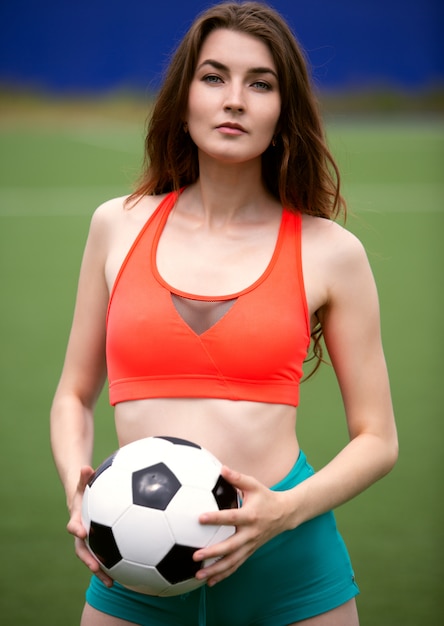 Een vrouwelijke voetballer in een top en korte broek heeft een bal in haar handen