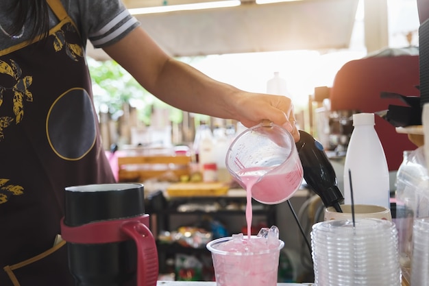 Een vrouwelijke werknemer giet roze melk in een plastic beker voor klanten.