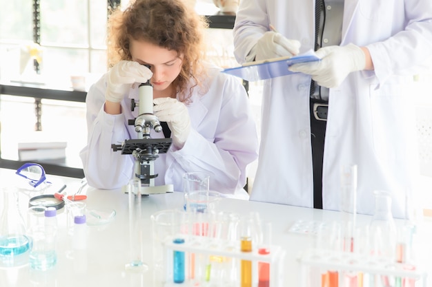 Een vrouwelijke wetenschapper die een microscoop bekijkt Mannelijke wetenschappers die testresultaten in de ochtend in het laboratorium registreren