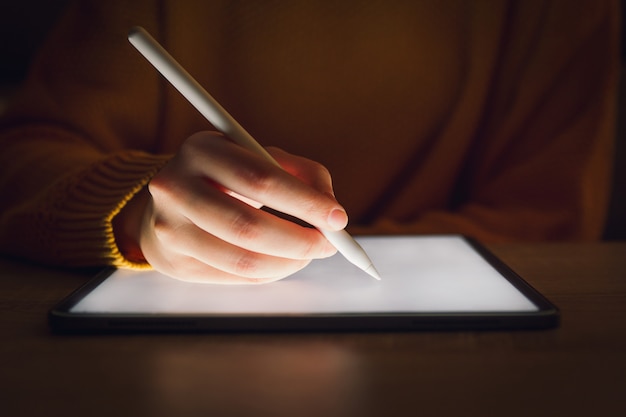 een vrouwenhand die in het donker op een tablet schrijft