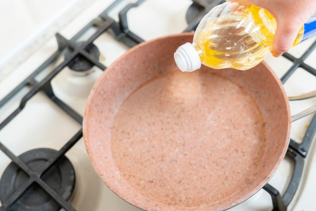 Een vrouwenhand giet thuis bakolie op de pan