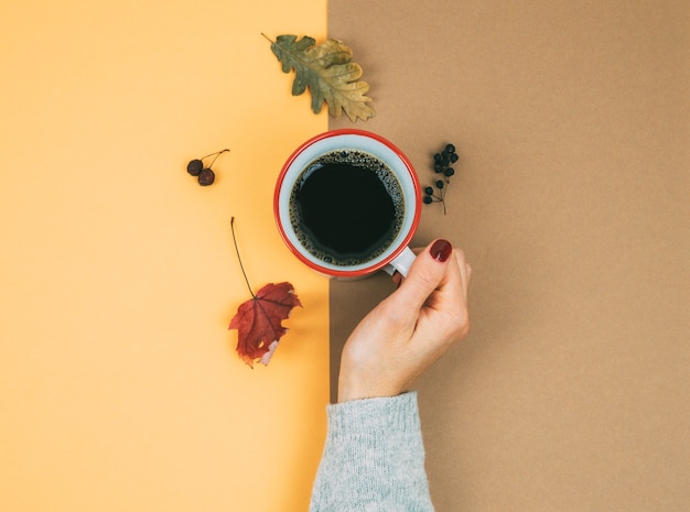 Een vrouwenhand met een kopje koffie en gedroogde bladeren. Herfst concept.