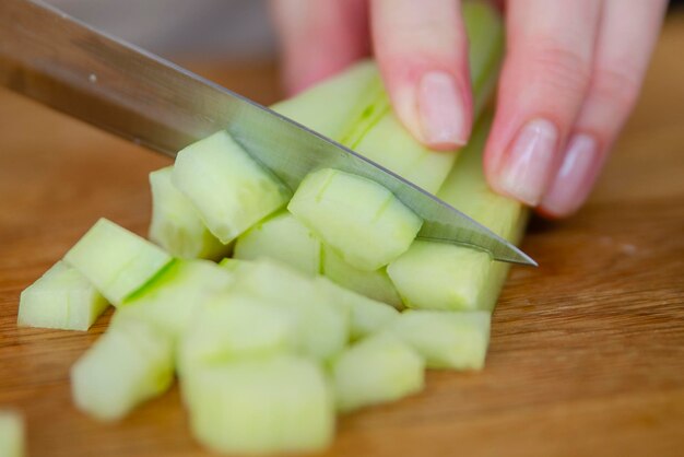 Een vrouws handen snijden een groene komkommer in kleine plakjes closeup lange groene komkommer plakjes zijn