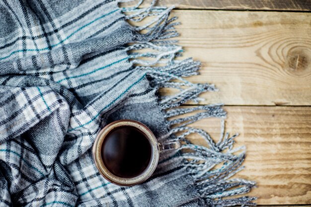 Een warme geruite sjaal met franje ligt op een lichte houten achtergrond Een glazen mok met zwarte koffie