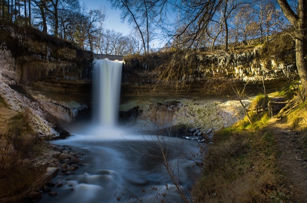 Een waterval in het bos met daarachter een blauwe lucht