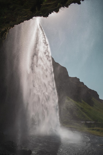 Foto een waterval in ijsland met een groene berg op de achtergrond.