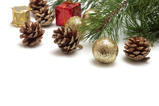 Een weelderige dennentak, dennenappels versierd met gouden glitter, glanzende gouden ballen, een speelgoedtrommel, een geschenk in een rode verpakking op een witte achtergrond. Sjabloon voor wenskaart of uitnodiging.