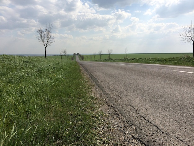 Foto een weg door een veld tegen een bewolkte hemel.