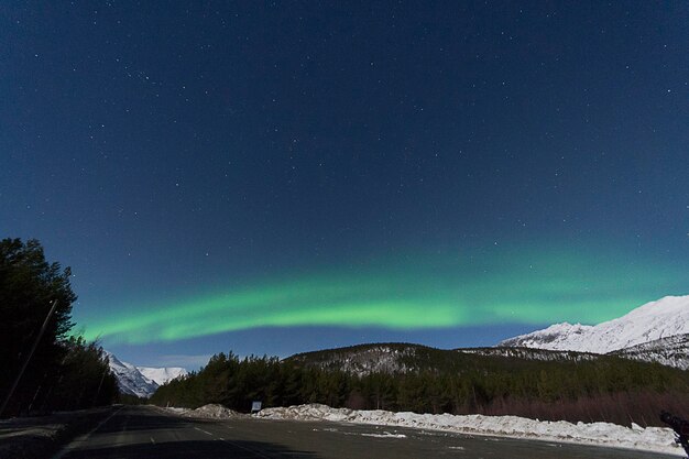 Een weg langs besneeuwde bergen tegen de aurora borealis's nachts