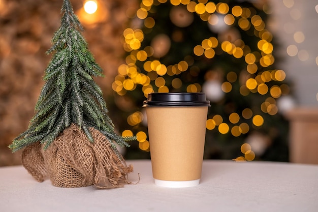 Een wegwerpkoffiekopje met deksel op de achtergrond van een kerstboom Plaats voor reclame