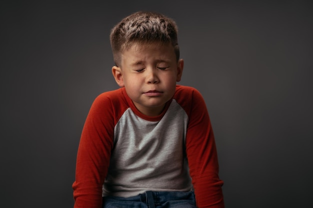 Een wens doen kleine jongen in rood en wit overhemd zit op de stoel met gesloten ogen en doet een wens voor c...