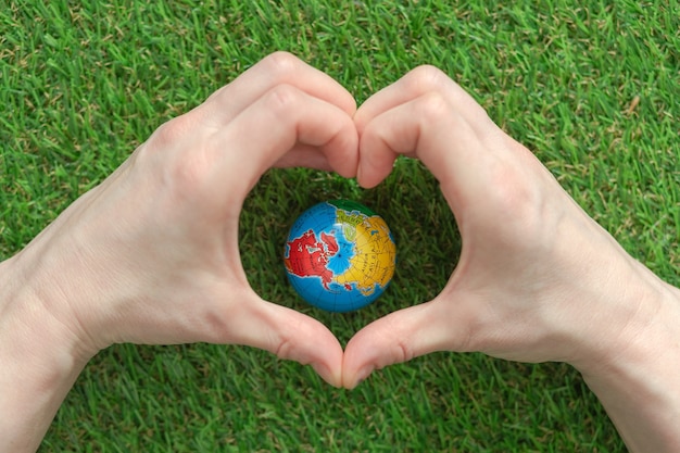 Een wereldbol op het weelderige groene gras, handen in de vorm van een hart. Dag van de Aarde. Planeet aarde