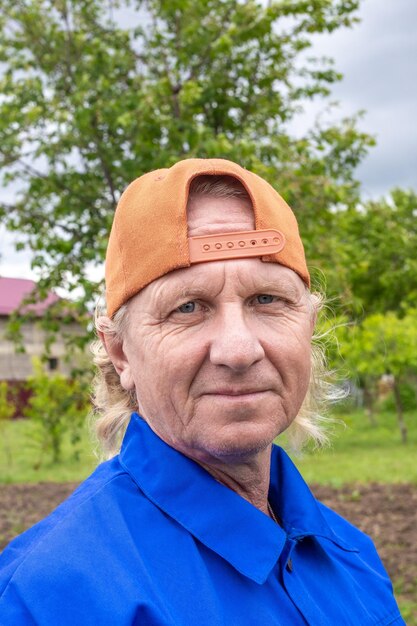 Een werkende man in een blauwe jas en pet kijkt naar de camera in een tuin in de zomer Portret van een blanke man