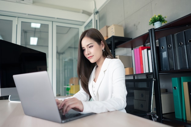 Een werkende vrouw in witte pak werkt op kantoor.