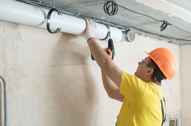 Een werknemer bevestigt ventilatiepijpen aan het plafond met een schroevendraaier